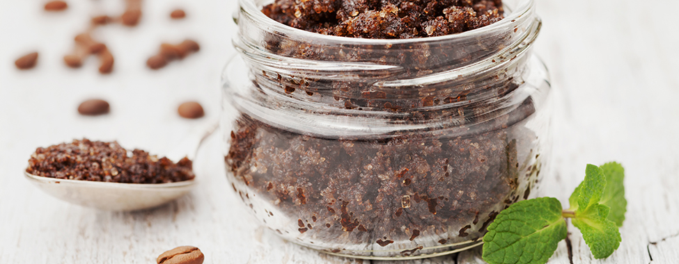 Body scrub of ground coffee, sugar and coconut oil in glass jar on white rustic table, homemade cosmetic for peeling and spa care