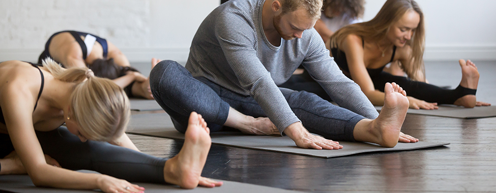 Group of young sporty people practicing yoga lesson with instructor, sitting in Janu Sirsasana exercise, Head to Knee Forward Bend pose, working out, indoor, studio. Wellbeing, wellness concept