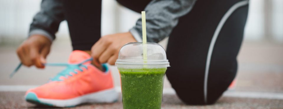 Detox smoothie drink and running footwear close up. City outdoor workout and fitness healthy nutrition concept.  Female athlete tying sport shoes laces before training.